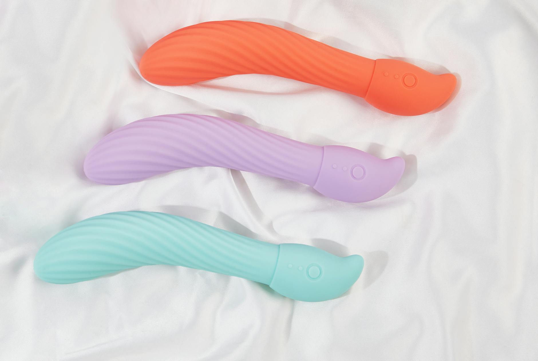 Three colorful vibrators arranged on white fabric, showing smooth texture and design