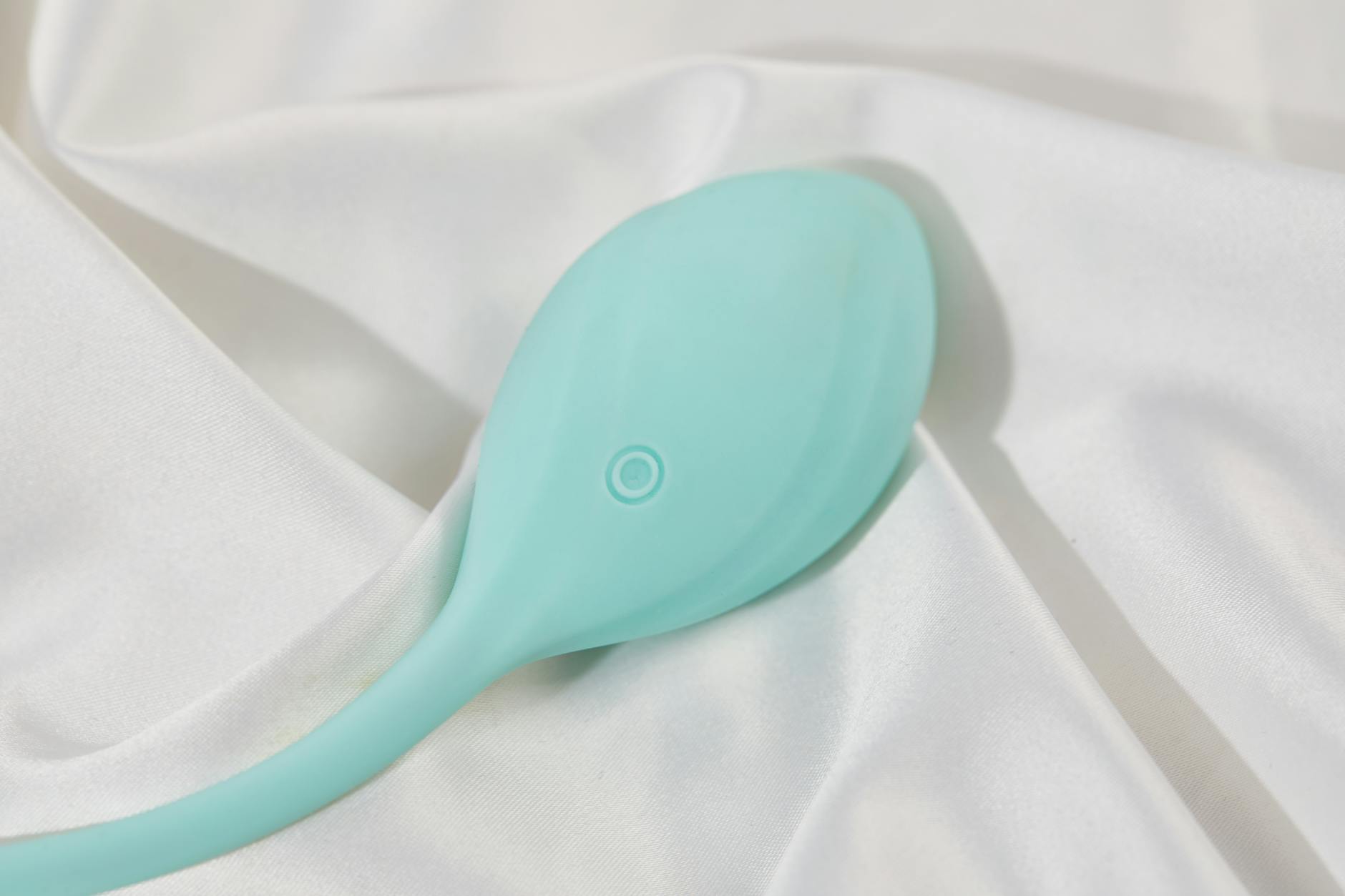 A stylish teal clitoral vibrator on smooth white silk, representing self-care and intimate recovery