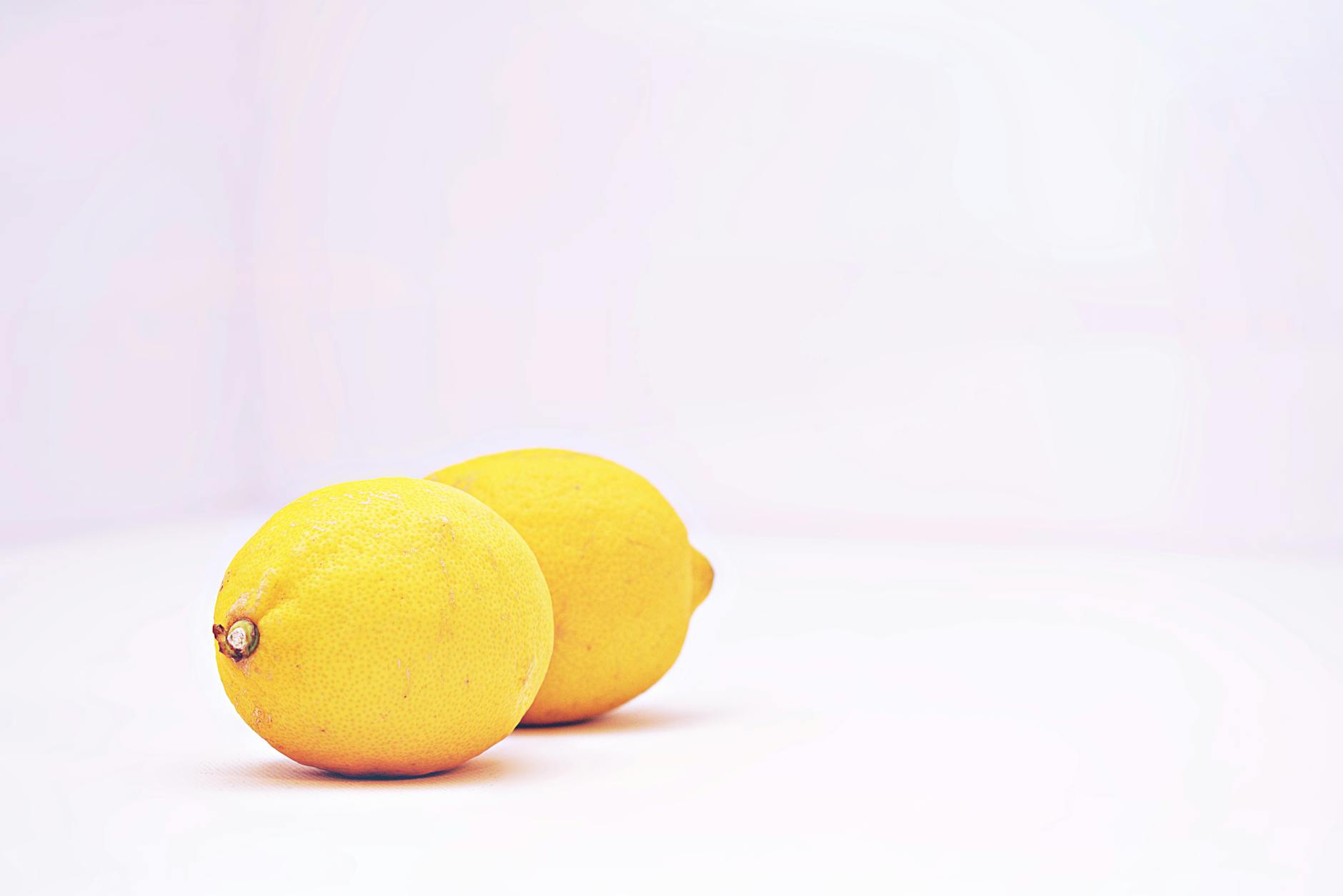 Hand holding a fresh lemon on soft pink background, representing natural pleasure and vitality