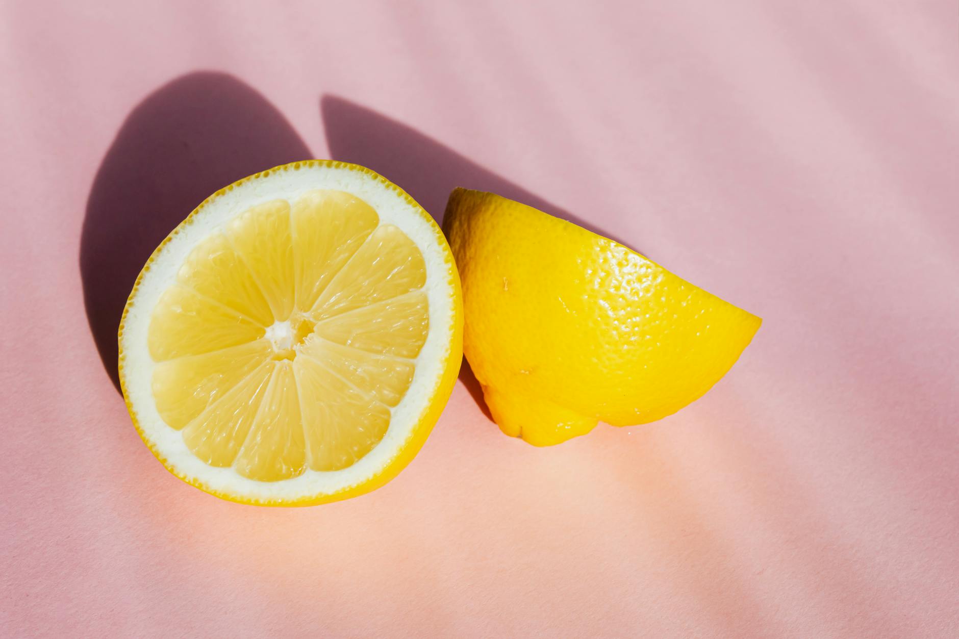 Fresh lemon halves on a pink background in sunlight, symbolizing freshness and vitality after menopause