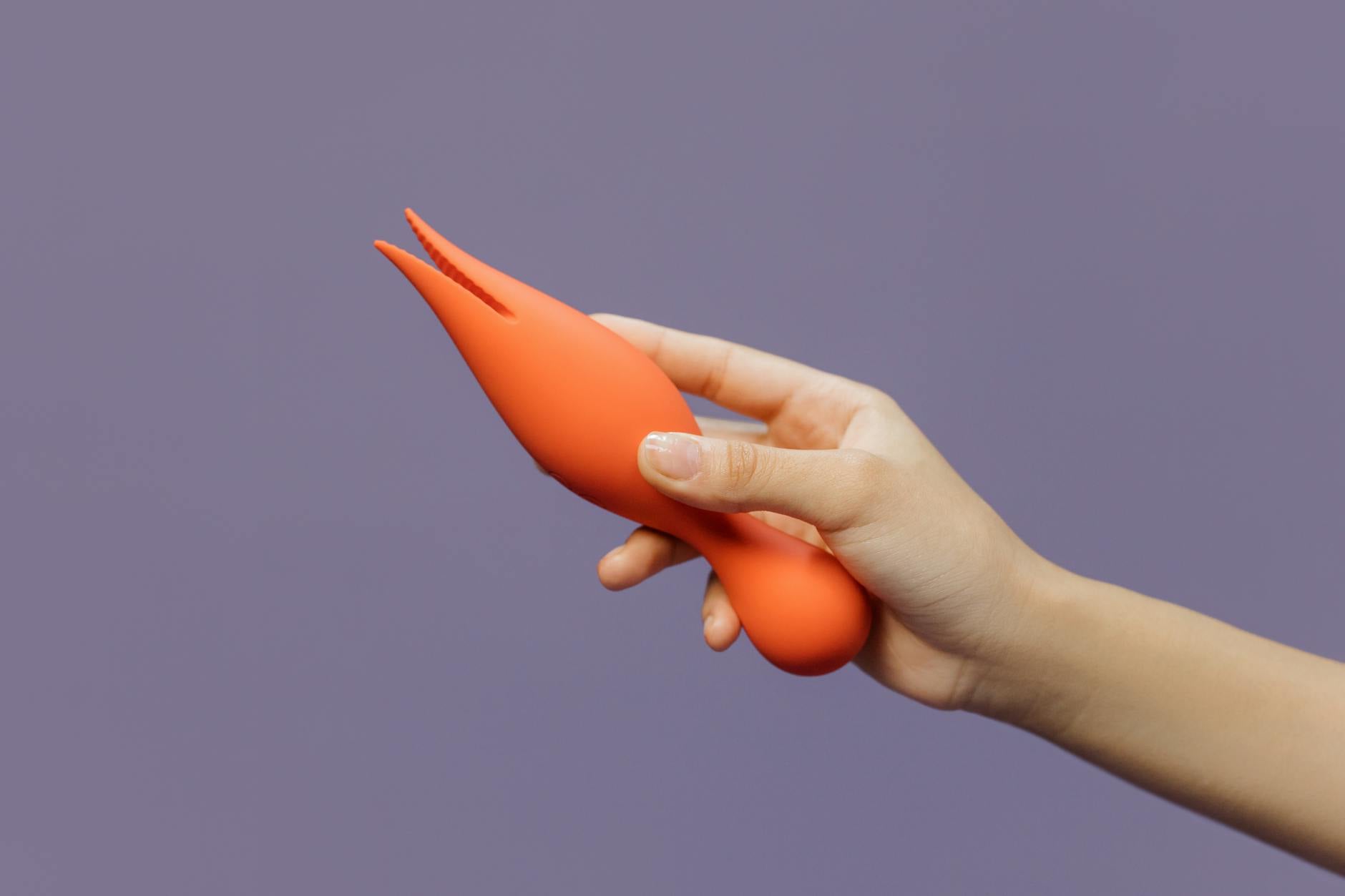 Hand holding a vibrator against a purple backdrop, showcasing modern sensuality and intimate wellness.