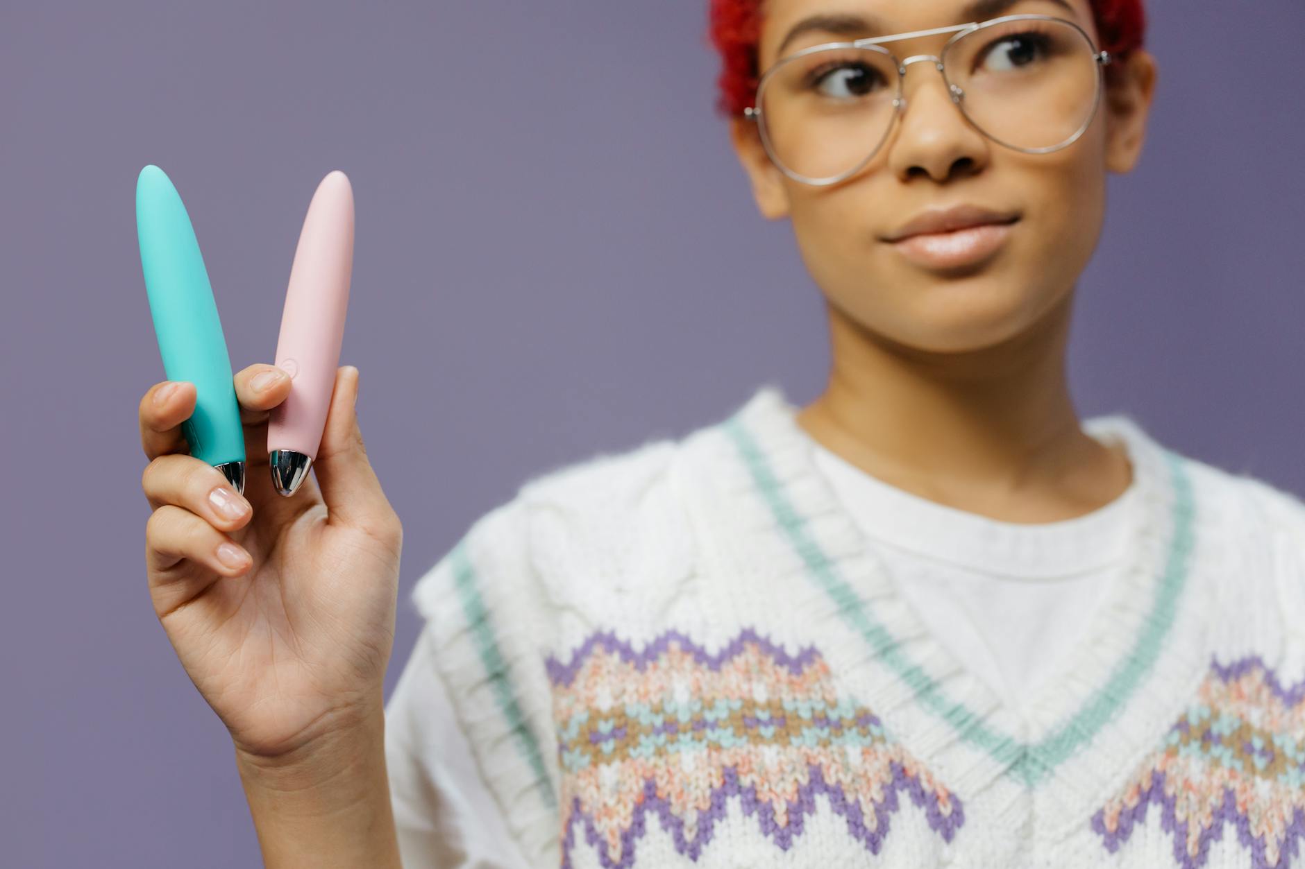 A woman holds colorful vibrators against a purple background, representing choice and agency in sexual wellness.