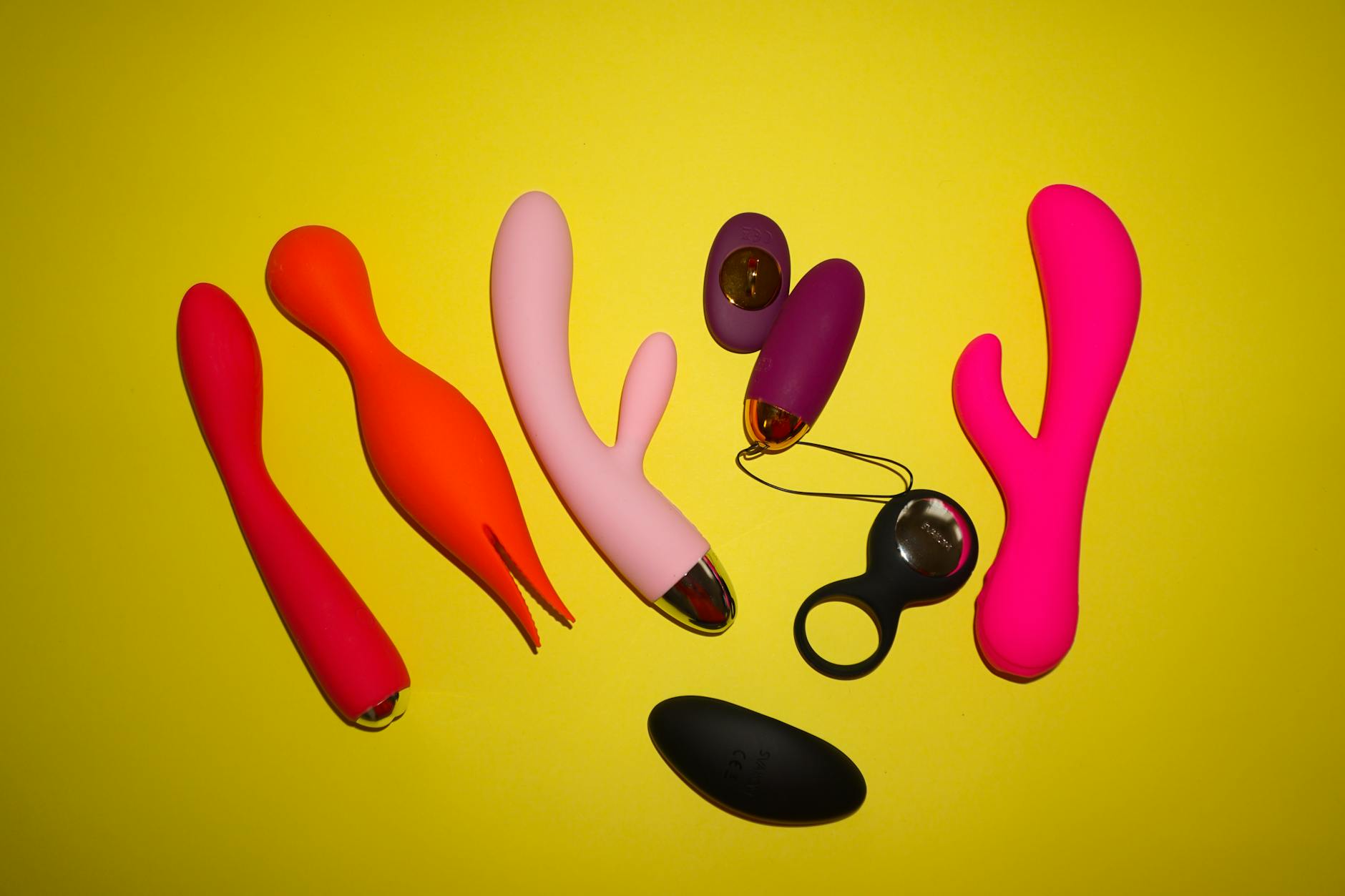 Colorful clitoral vibrators arranged on a bright yellow background, showcasing various shapes and designs