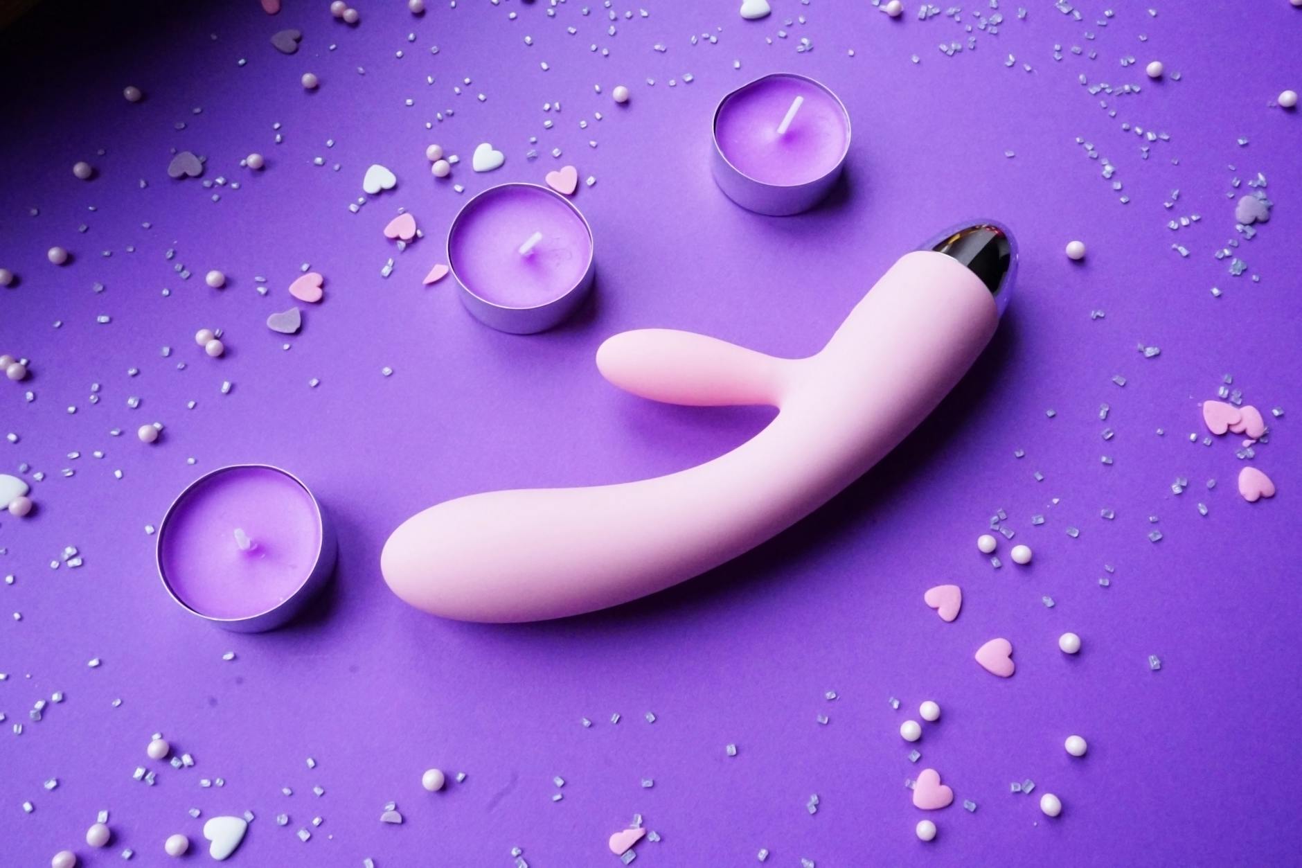 A pink vibrator on a purple background with heart confetti and candles for romantic intimacy